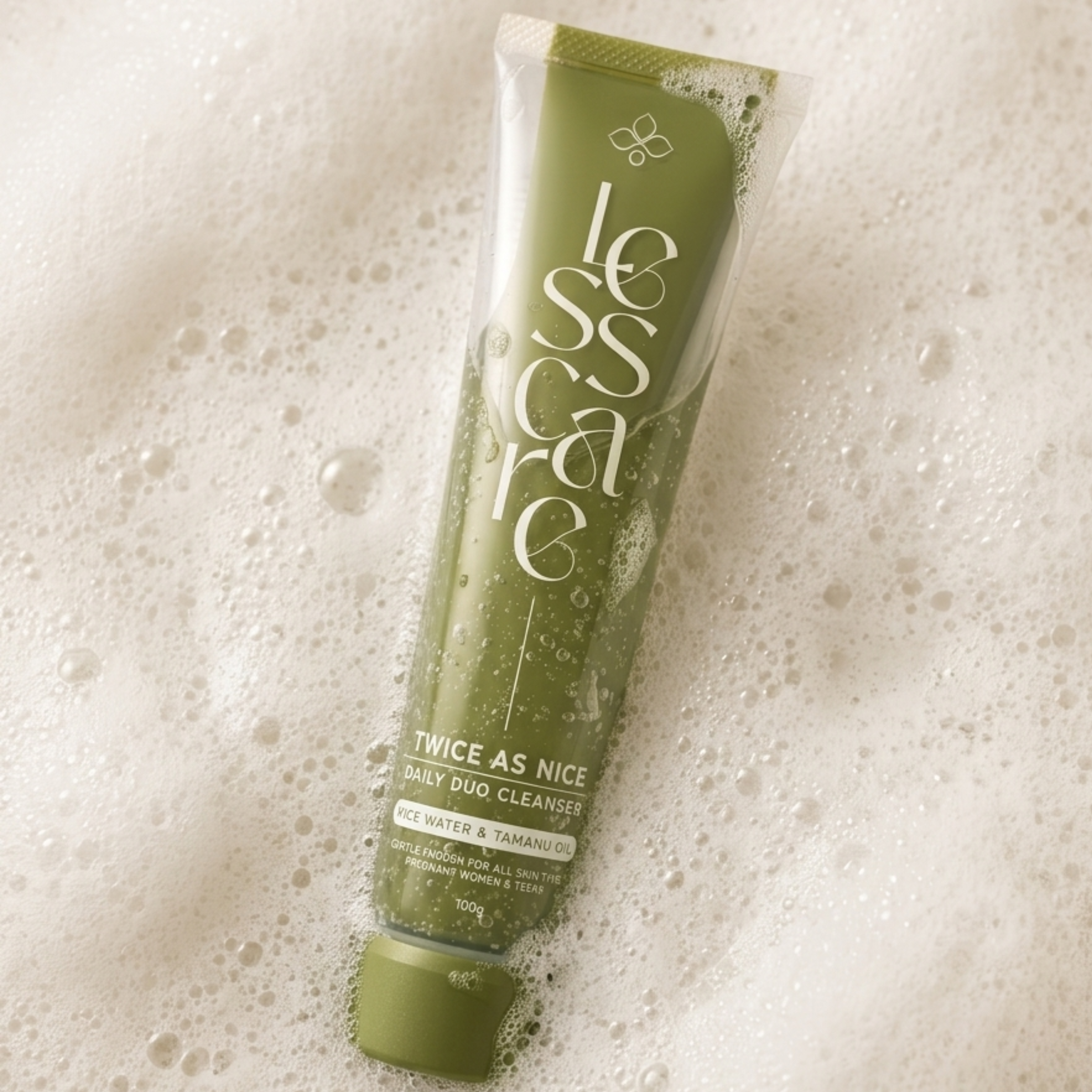 A squeeze tube of Less Care Twice As Nice Daily Duo Cleanser resting diagonally on a bed of white foam bubbles.